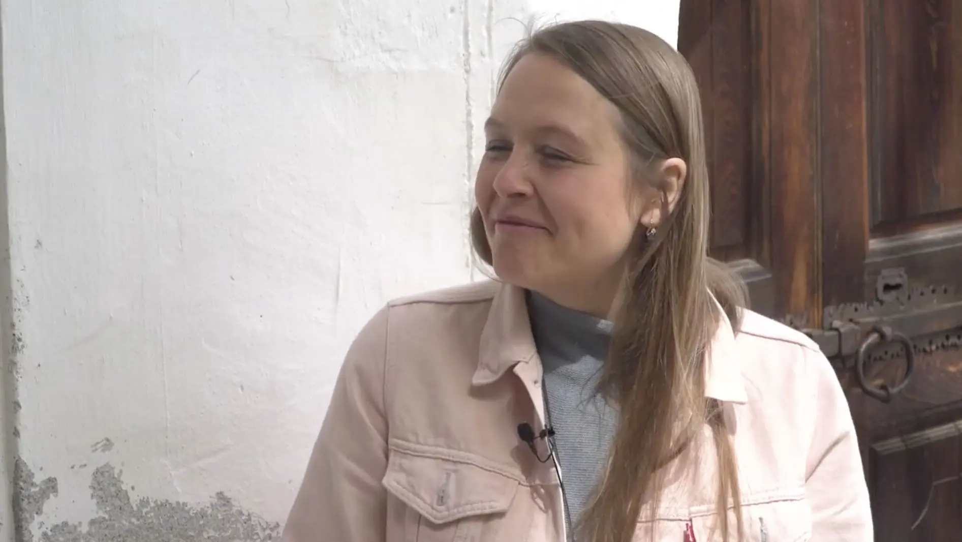Renata Luminati con lunghi capelli castani, vestita con una giacca rosa chiaro, sorride mentre guarda verso destra. Sullo sfondo si intravede un muro bianco.