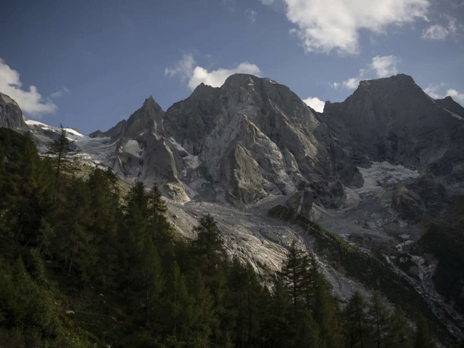 Imponenti montagne con cime rocciose e una coltre di ghiaccio, circondate da alberi verdi e un cielo parzialmente nuvoloso.