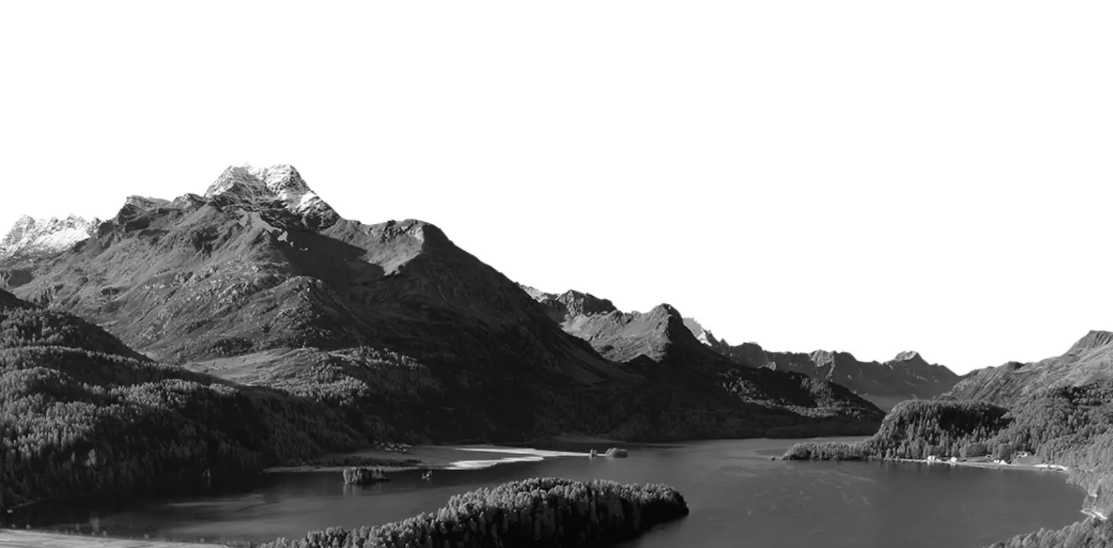 Panorama montano in bianco e nero con un lago circondato da alberi e montagne. Le cime delle montagne sono parzialmente innevate, creando un contrasto con il cielo chiaro.