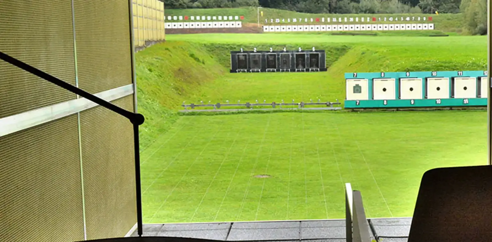 Vista di un campo di tiro con bersagli sullo sfondo. L'area è verde e ben curata, con diversi bersagli disposti lungo una collinetta. Una rampa in primo piano conduce verso il campo.