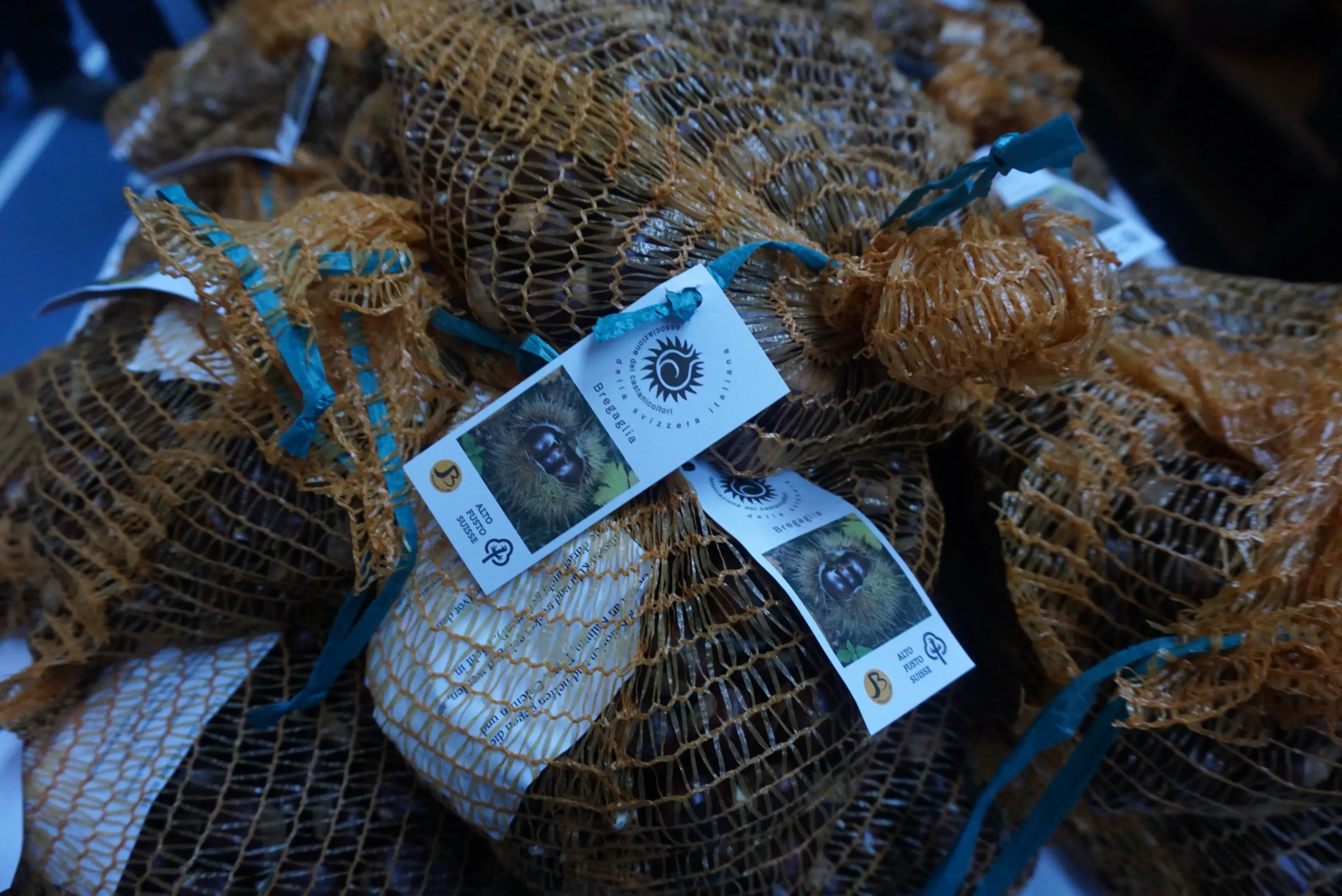 Sacchetti di molluschi in rete arancione, ciascuno etichettato con informazioni sul prodotto e un logo.