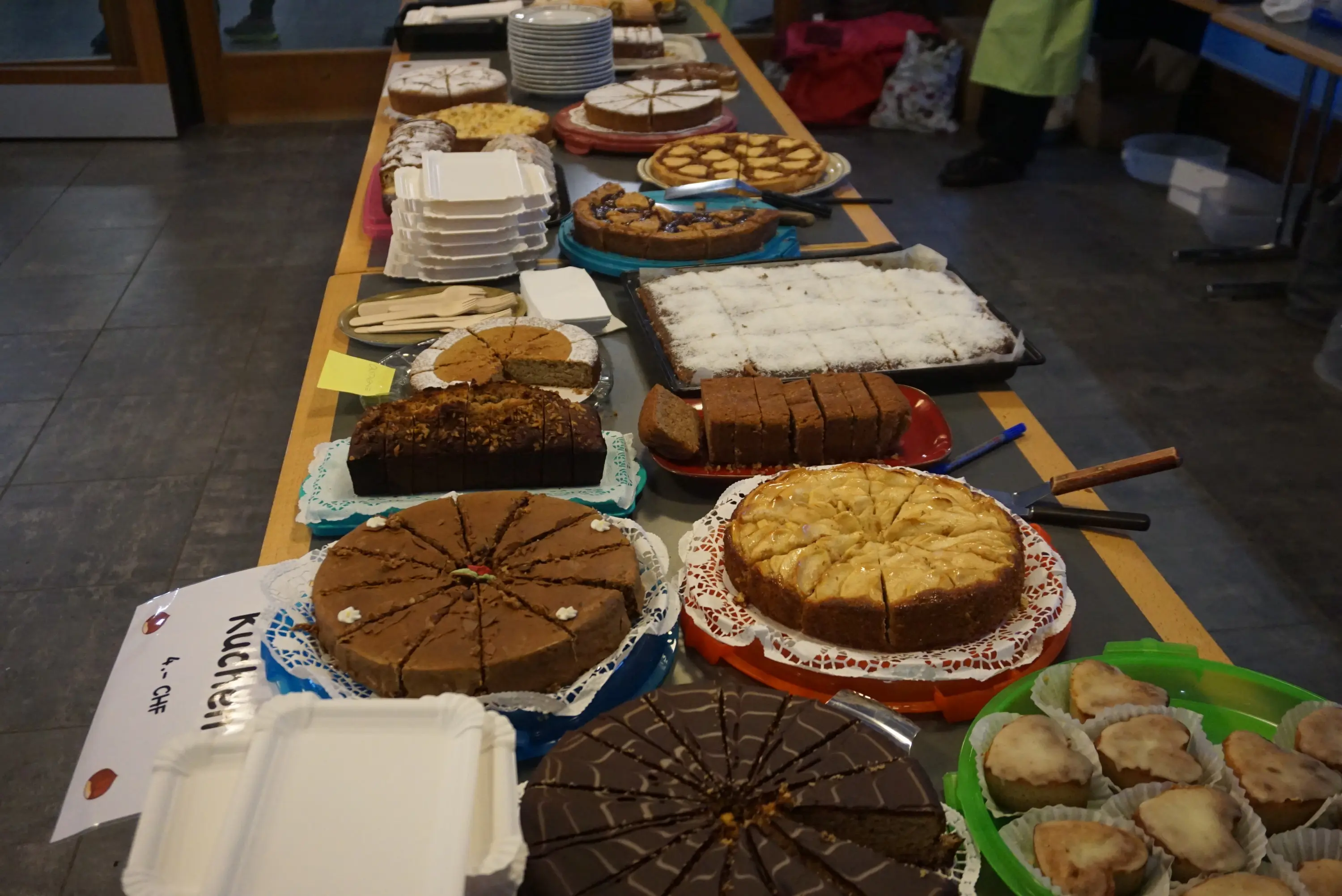Un tavolo allestito con una varietà di dolci, tra cui torte, biscotti e dessert assortiti, disposti su piatti e vassoi. Alcuni dolci sono decorati con glassa o frutta.