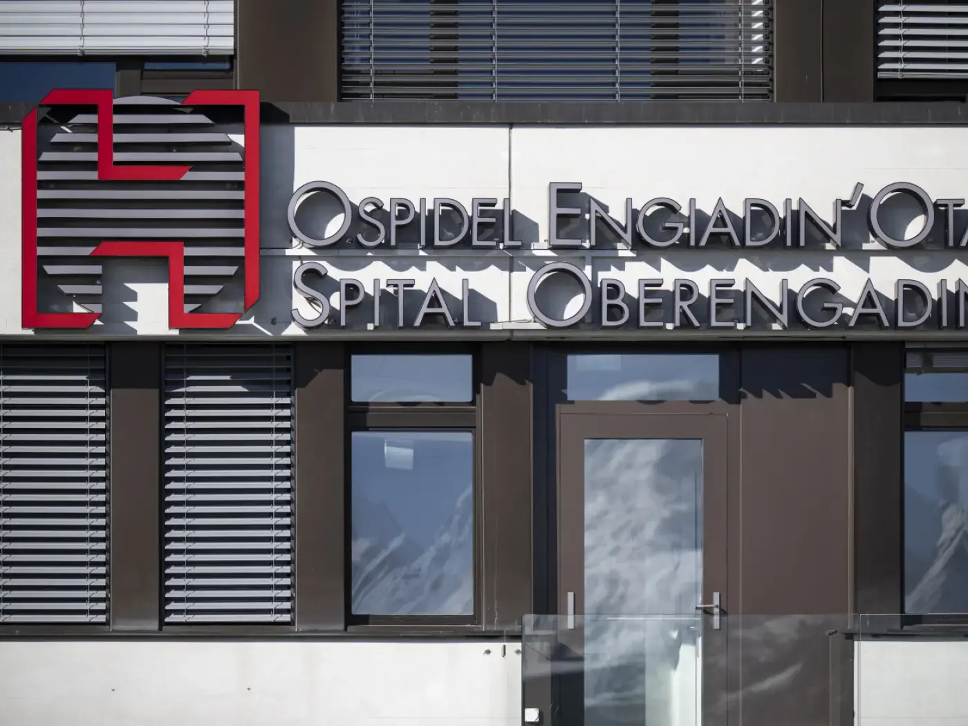Insegna di un ospedale con il logo rosso e il testo "Ospidel Engiadin-Ot Spital Oberengadin" su una facciata moderna.