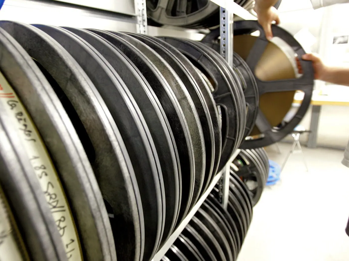 Rulli di pellicola cinematografica conservati su scaffali, con una persona che ne sta estraendo uno.