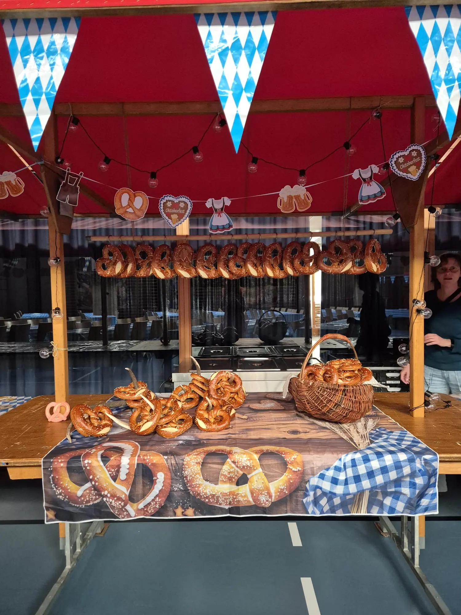 Banco di un mercato con una selezione di pretzel appesi e disposti su un tavolo. Decorazioni a tema bavarese con bandierine e immagini di pretzel. Una persona è visibile dietro il banco.