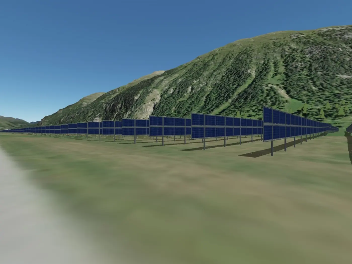 Campo di pannelli solari all'aperto, situato su un terreno collinare, con montagne verdi sullo sfondo. Il cielo è sereno e blu.