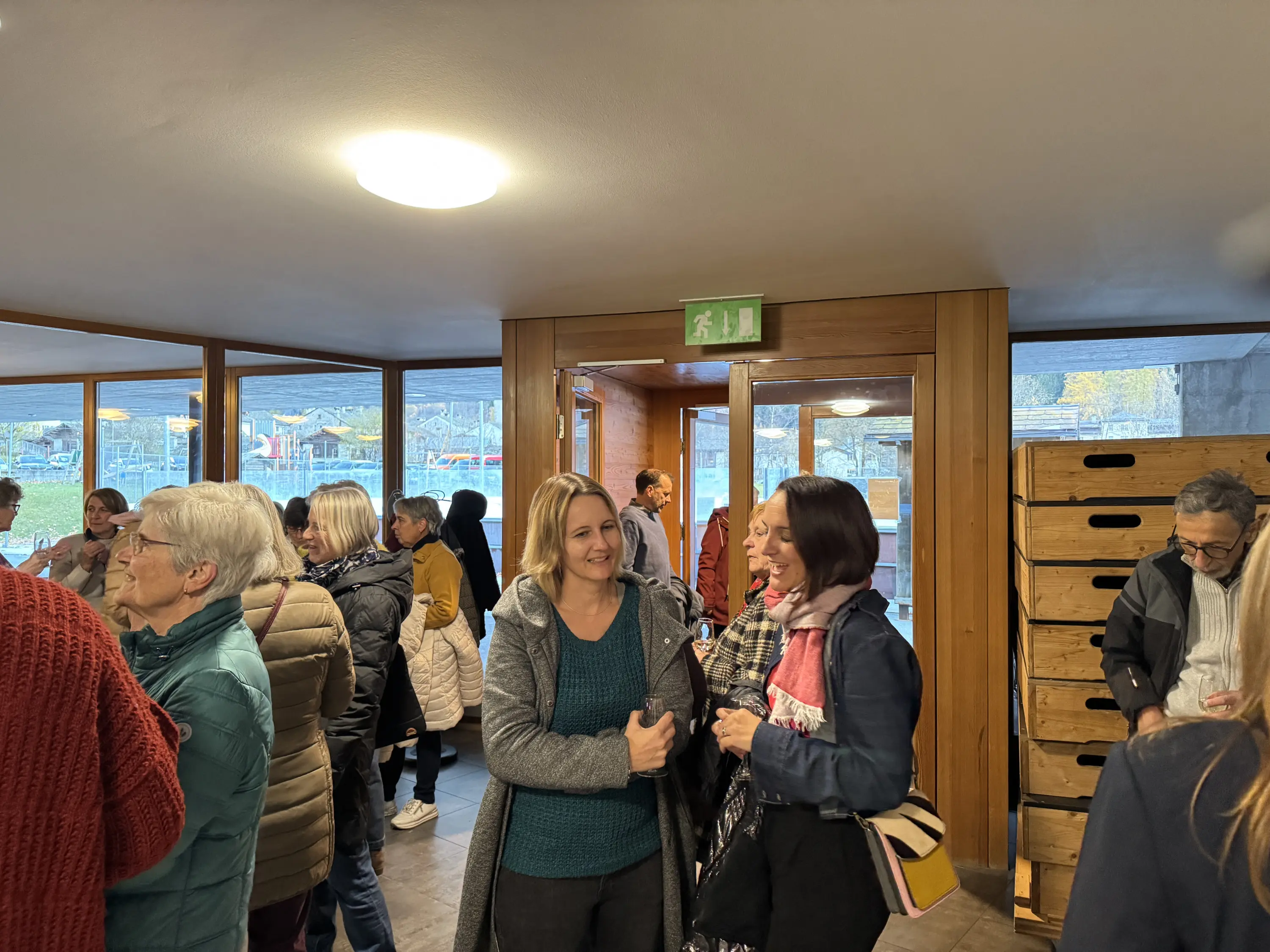 Un gruppo di persone si riunisce in un ambiente accogliente e luminoso, con alcune conversazioni animate. Sullo sfondo, si intravedono finestre che offrono una vista sul panorama esterno.