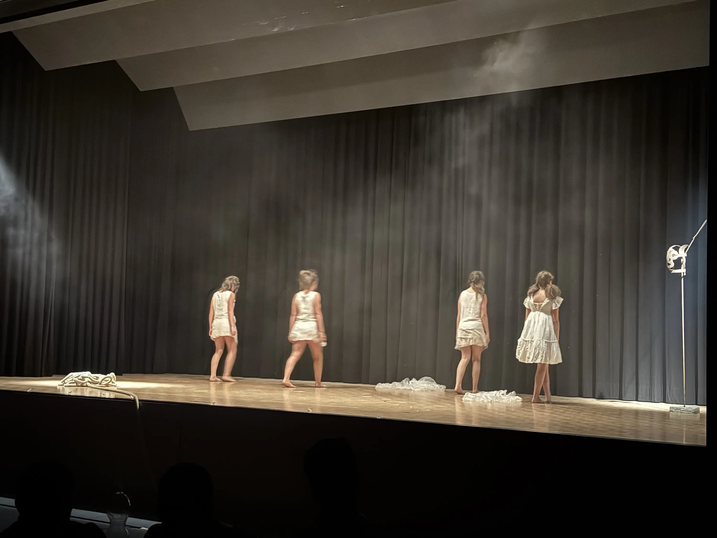 Gruppo di ballerine in abiti bianchi che si esibiscono su un palcoscenico con sfondo scuro e fumi leggeri.