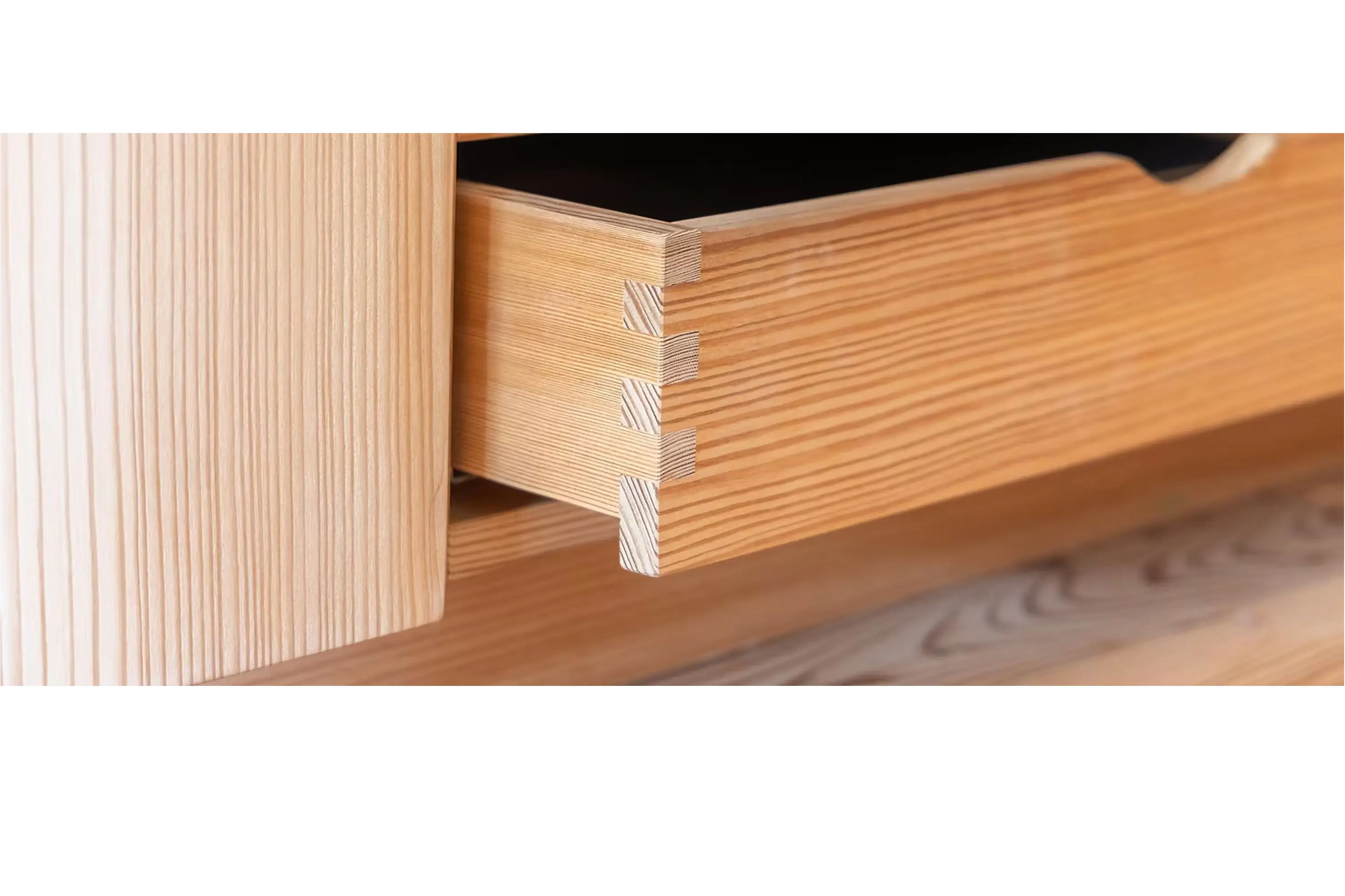 Dettaglio di un cassetto in legno chiaro con giunzioni a coda di rondine, aperto e posizionato su una base di legno.